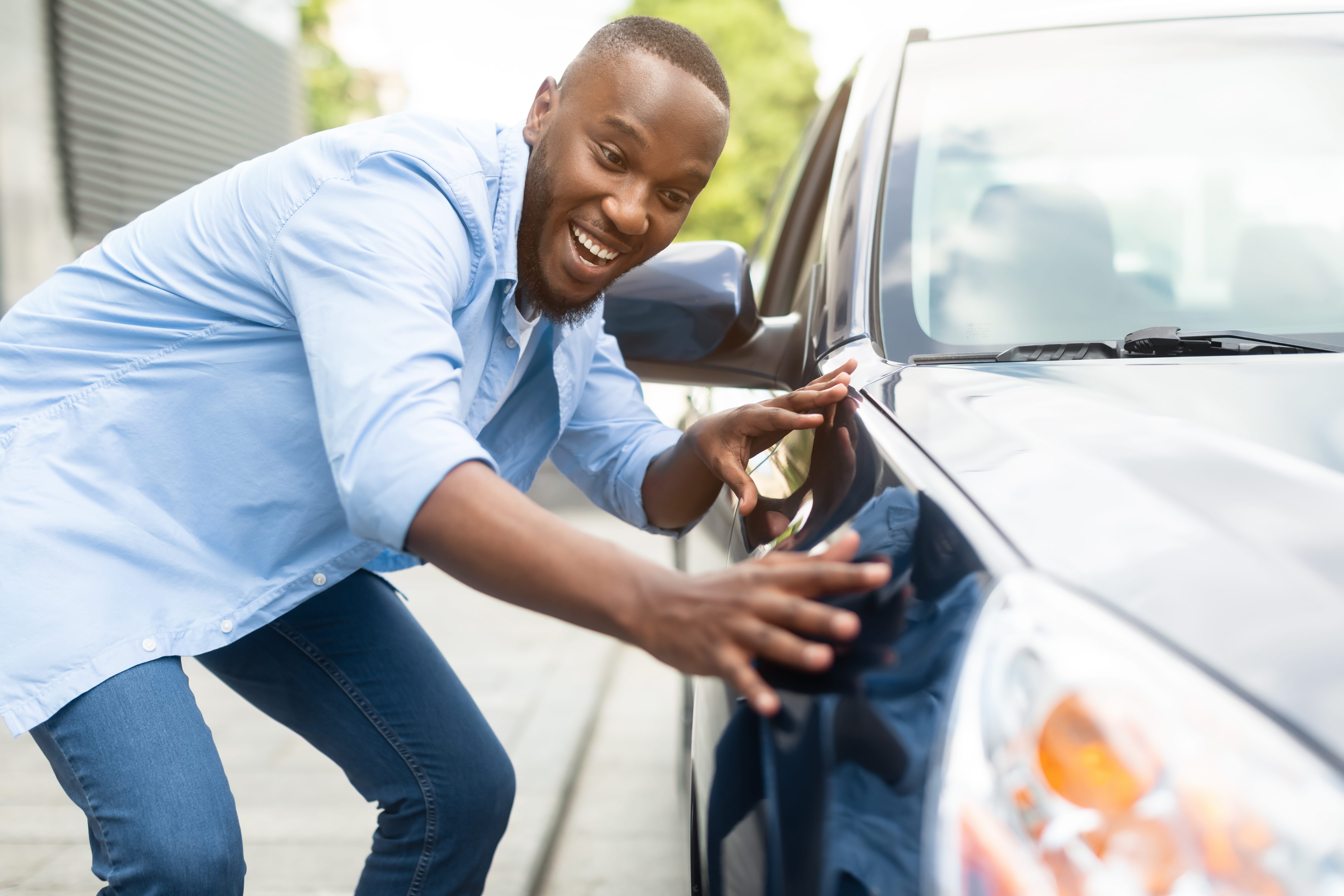 Happy Car Buyer, New Car Owner Concept. Portrait Of Excited Young African American Guy Touching His New Luxury Automobile After Purchase In Dealership Showroom. Selective Focus